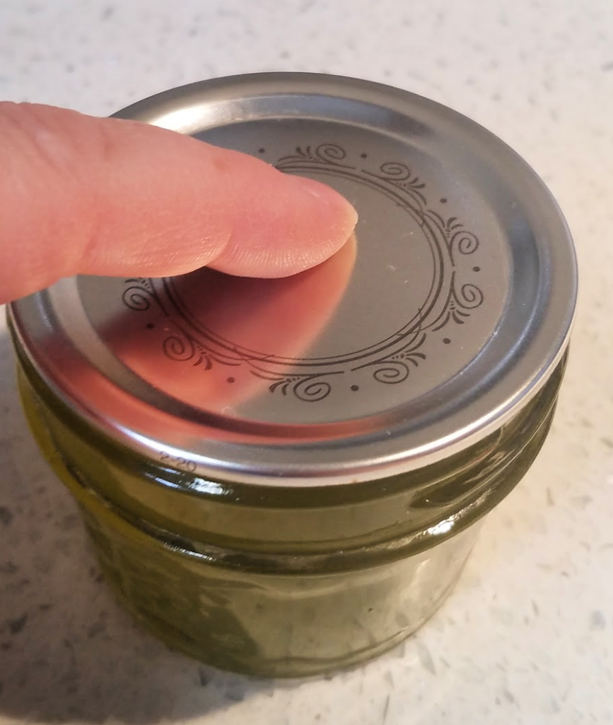 Finger centered on lid on canning jar