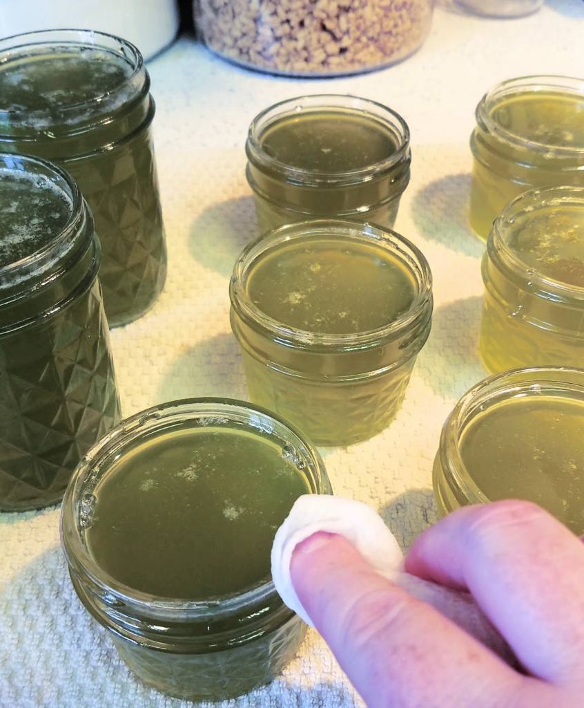 hand wiping rims of green pepper jelly jars with paper towel